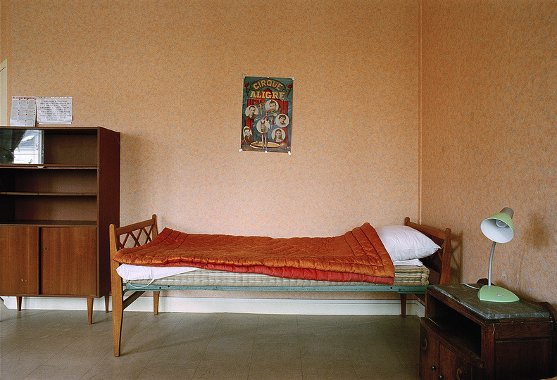 Mobility: In his photo series Chambres [Quarters](2005), Taysir Batniji presents views of temporary quarters for Renault factory employees in France. These are furnished in a way that is extremely functional and also sparse. These short to middle term residences offer shelter and lodgings and thus stand for the transitory spaces of the international diaspora, in this case voluntary (and paid) migration. They also act as proxies for the many transitional spaces that refugees, people searching for a better life or simply for work often encounter. Taysir Batniji, from the series  