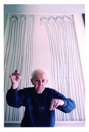 The Artists of Gugging: Artist Oswald Tschirtner standing in front of his work titled People, felt-tip pen on paper and wooden panel, 1980.