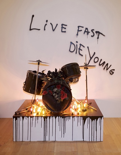 Urban Gothic: Teenage kicks, 2003.  Courtesy Upstream Gallery . Drum set covered with candle wax on stage with light bulbs, plastic flowers and skull, and spraypaint on wall.