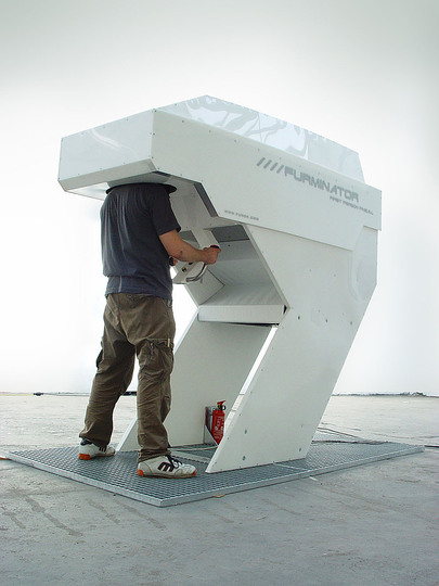 Weapons of Mass Distraction: The ////furminator is a pinball machine that puts the player in a first person perspective similar to modern “EGO Shooter” video games. Like being inside a huge VR-helmet, the player’s head is stuck into the ////furminator capsule. His nose is situated right behind the flipper fingers, only centimeters away from the ball. Sealed off from reality and with his head arrested inside a force-feedback-helmet, the sound- and lighteffects, the mechanical noises of the pinball and the absorbing perspective create a highly immersive mechatronic environment.

In the traditional pinball perspective – looking at the playfield from above – the perception of the gameplay is almost two-dimensional. The ////furminator however unifies the origin of visual perception and the physical vanishing point of the ball. Ceaselessly the ball is rolling towards the player’s face which is protected only by a small plastic screen. The high velocity of the approaching ball poses a constant threat to newbies, but the experienced ////furminator pilot will quickly appreciate the improved aiming possibilites the perspective provides.

 

The main idea behind behind the furminator was to create an immersive space which does not rely on computer generated images. Nowadays, the term “virtual reality” is instantly associated with rendered 3D graphics, projected onto walls surrounding the spectator or displayed on head-mounted LCD screens. Not only do most of these synthetically generated environments look non-real, they also leave most of the spectator’s senses outside in the real world.

By combining the perspective of an EGO-shooter with a mechanical pinball machine the ///furminator creates a “virtual reality” that incorporates the full body of the player. The “man against machine” setup provides an unparalleled experience and the interaction is not limited to pushing buttons: the whole body can be used to move and tilt the pinball until the ////furminator admonishes you to “chill out”.